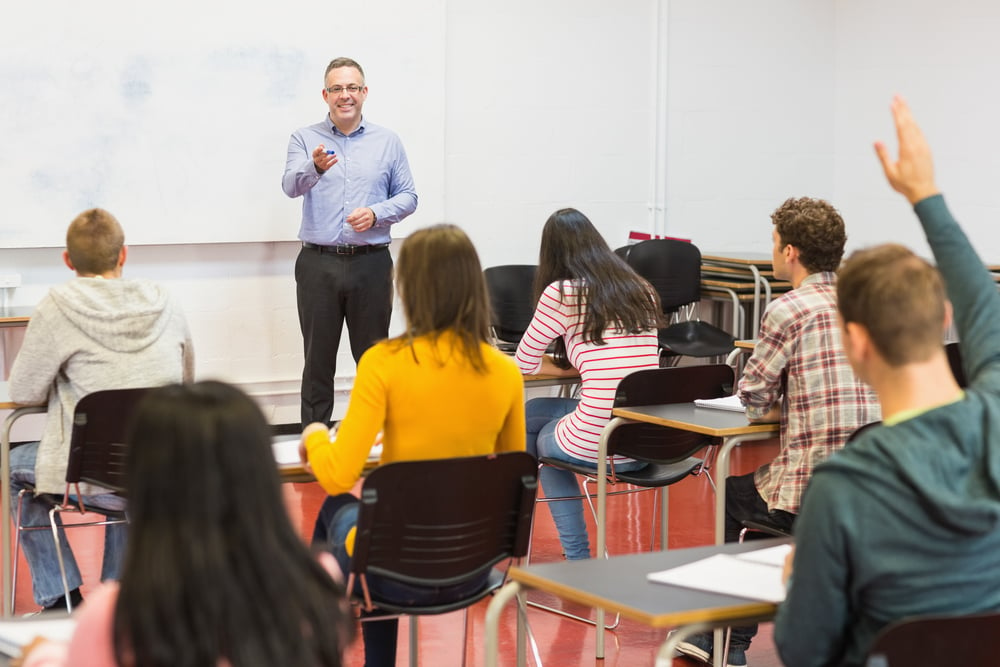 Rear view of students attentively listening to male teacher in the classroom